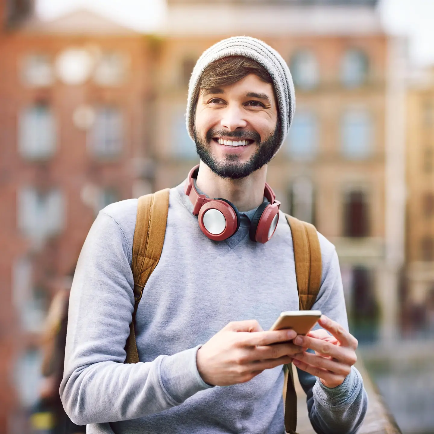 Un jeune homme riant avec des écouteurs et un smartphone à la main.