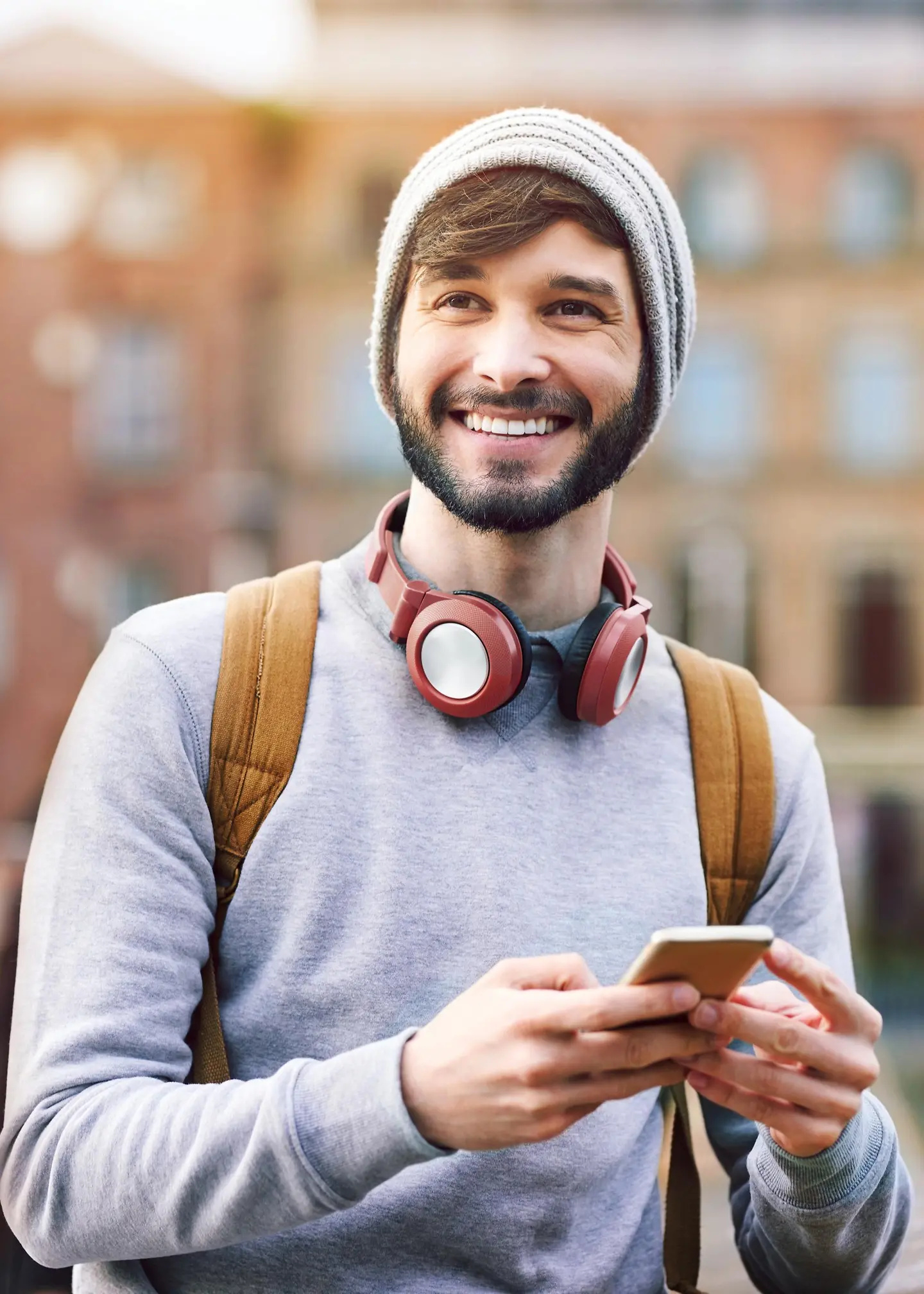 Un jeune homme riant avec des écouteurs et un smartphone à la main.