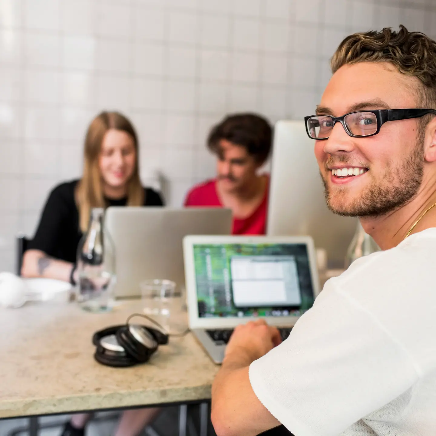 Un jeune homme au bureau, assis à son bureau et regardant dans la caméra.