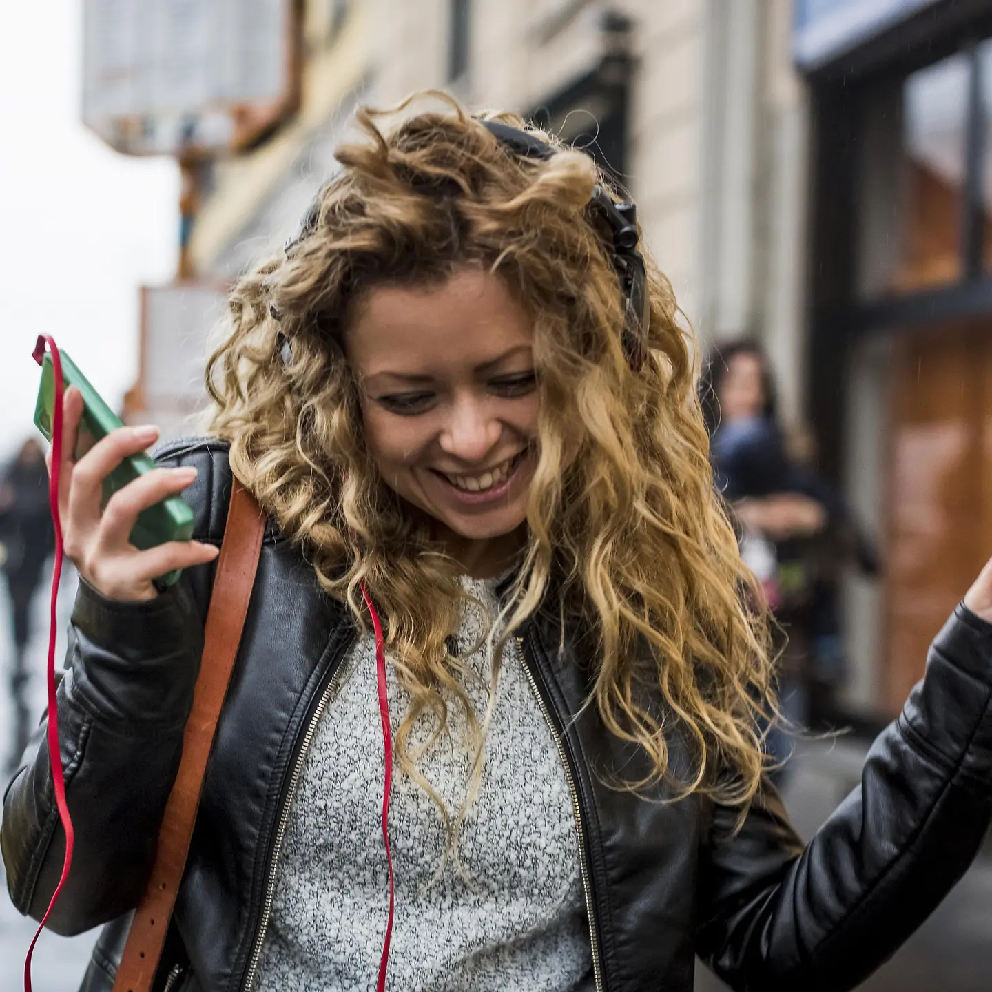  Une jeune femme marche dans la rue en riant et en écoutant de la musique sur son téléphone portable.