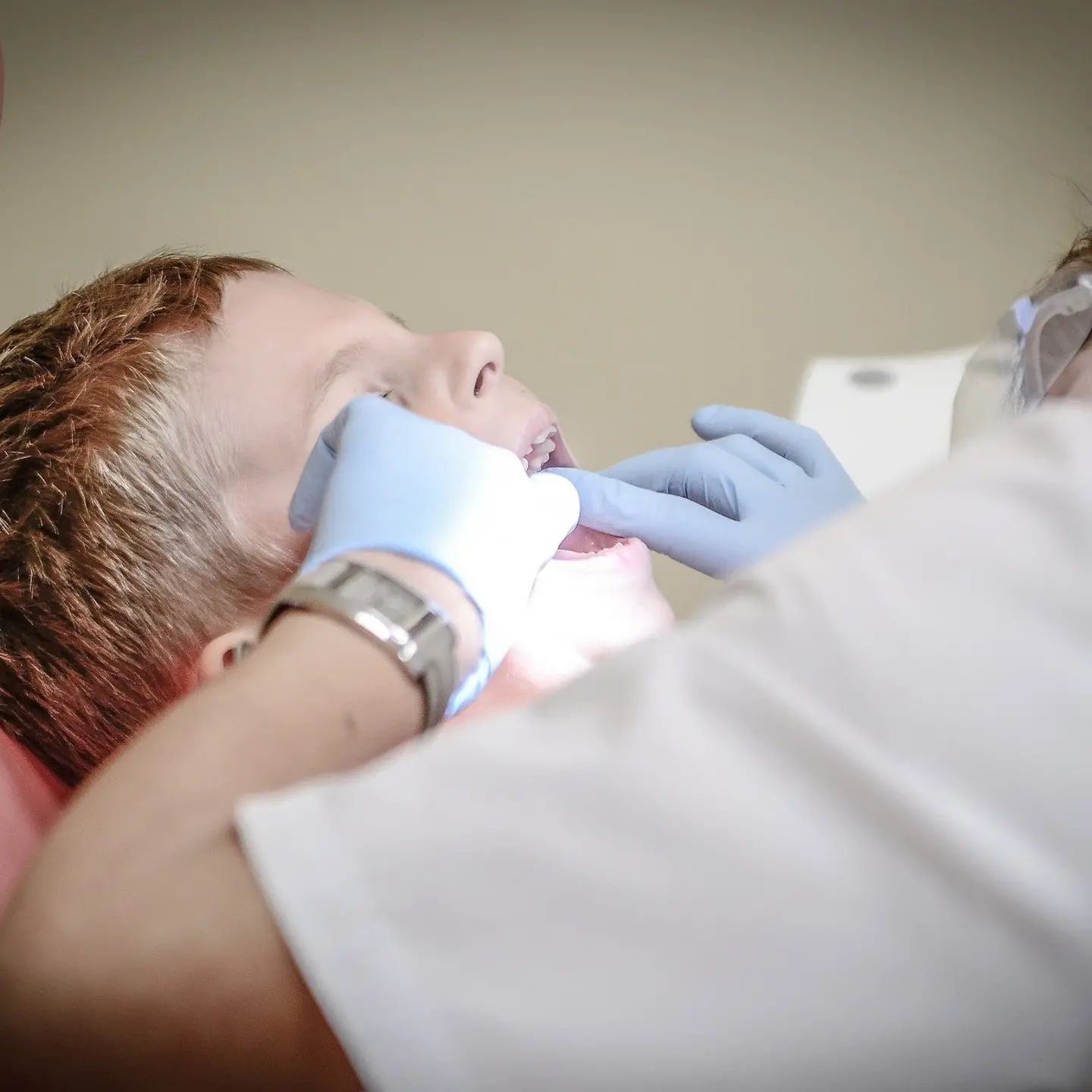 Ein Junge sitzt mit geöffnetem Mund auf einem Zahnarztstuhl. Eine Zahnärztin behandelt ihn.