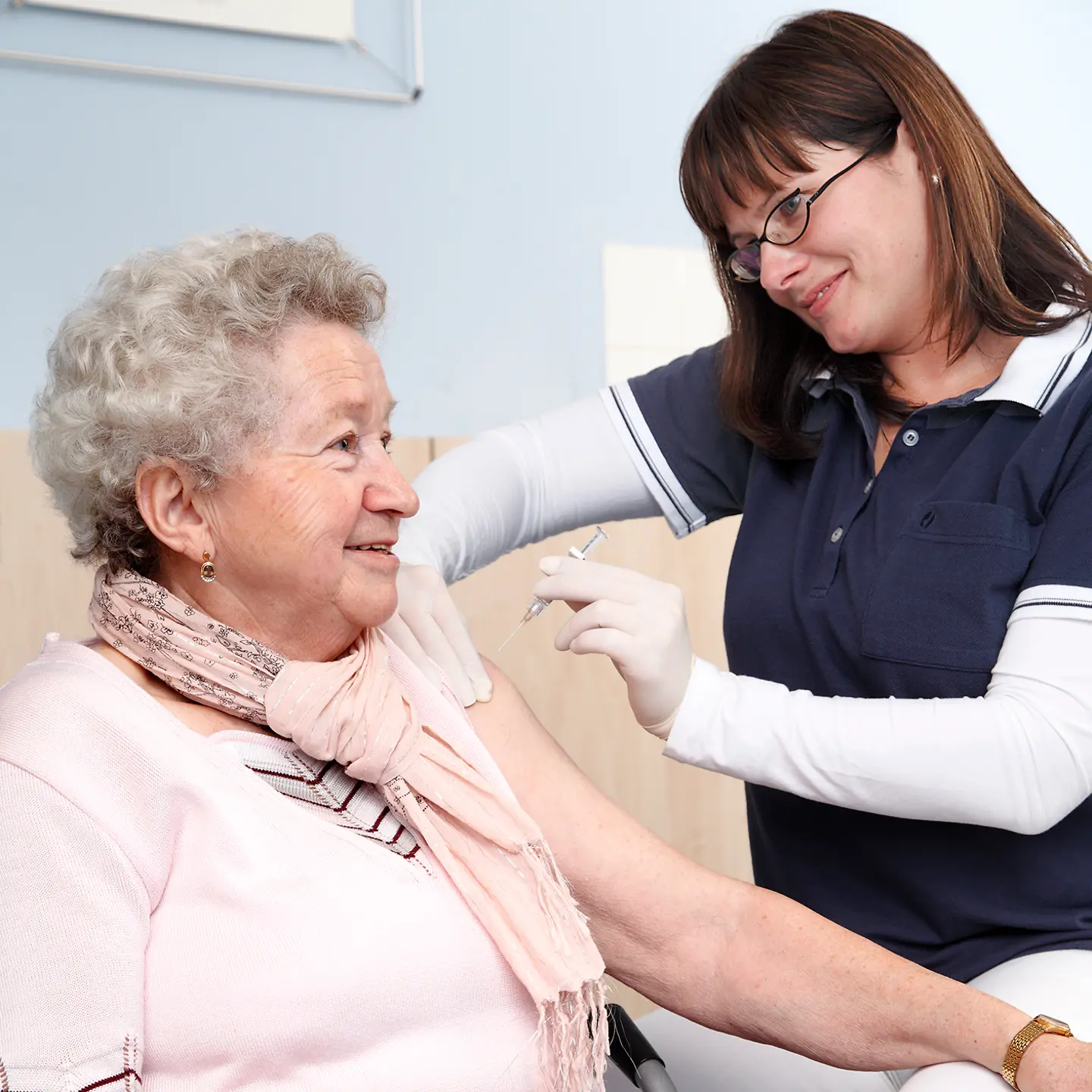 Eine ältere Dame erhält von einer Arzt-Schwester eine Impfung in den linken Oberarm