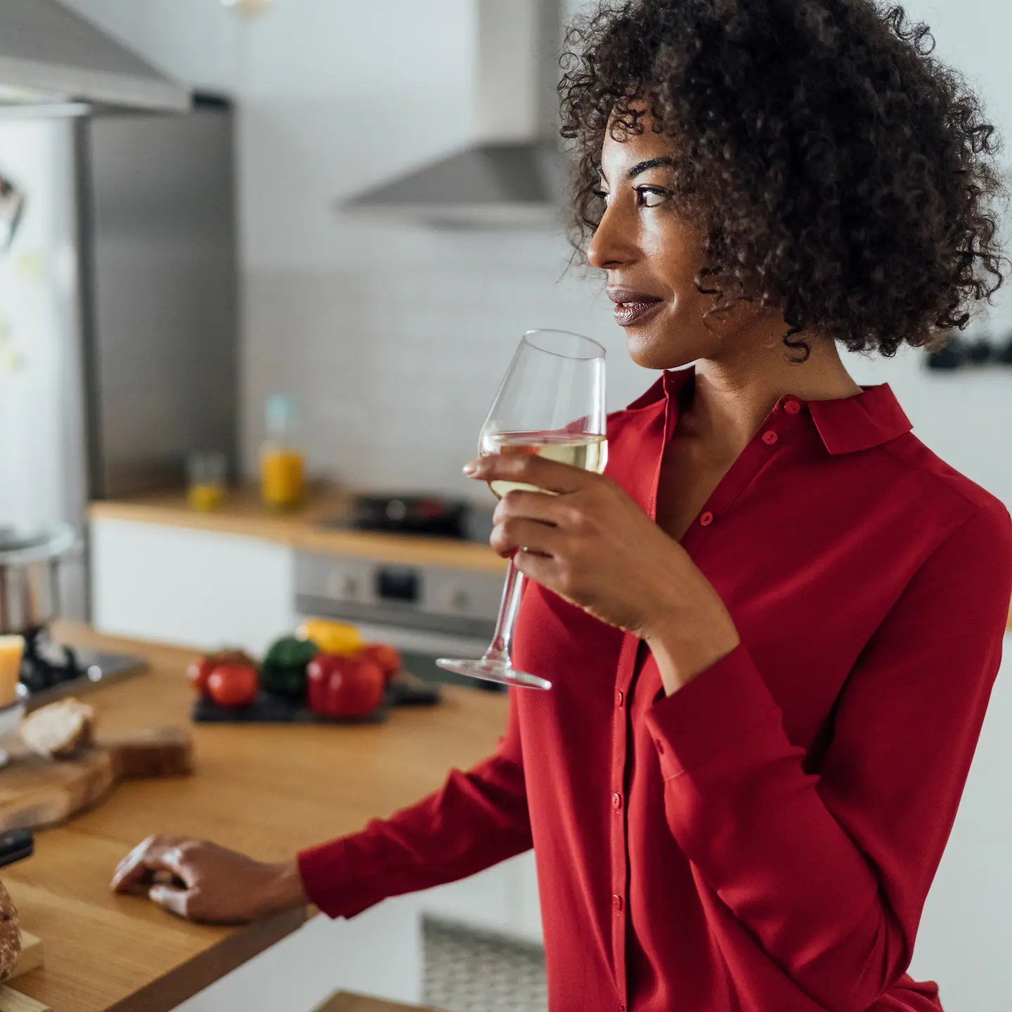 Eine Frau steht in der Küche und trinkt ein Glas Wein.