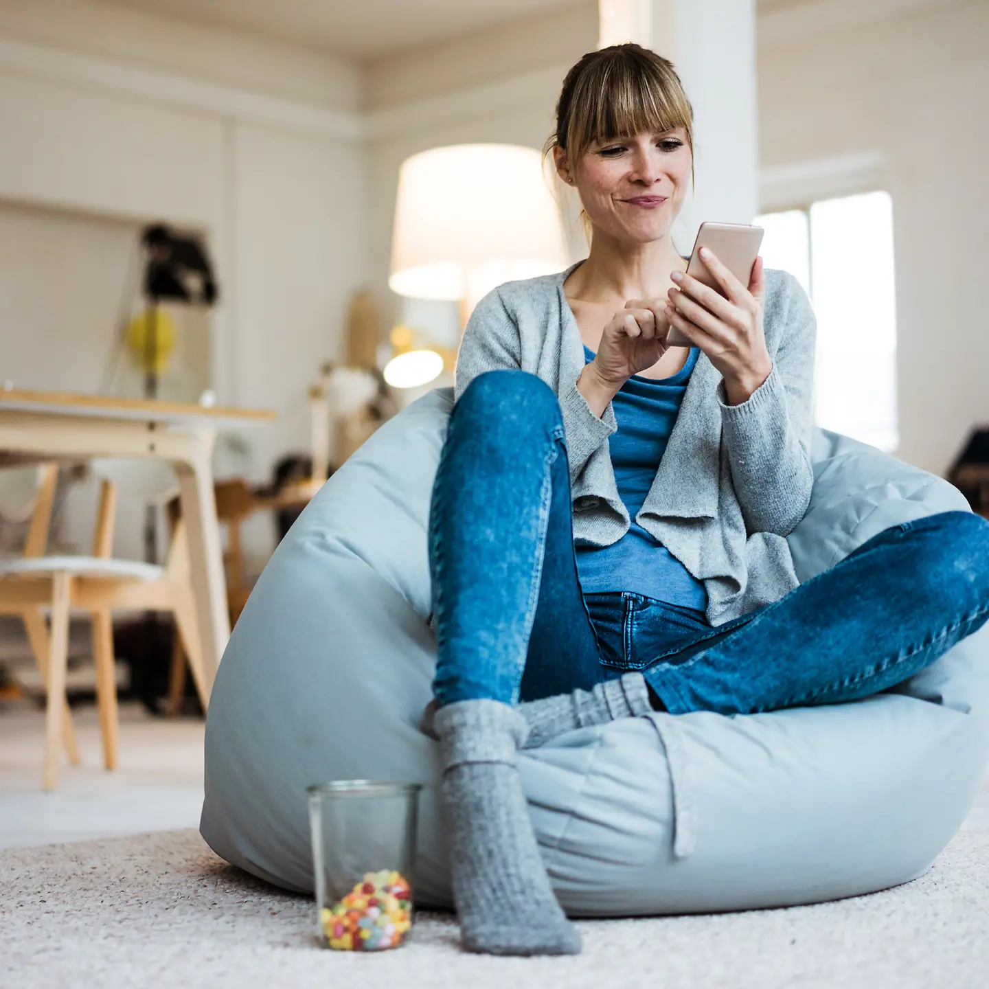Una mujer joven sentada en un puf mirando el móvil
