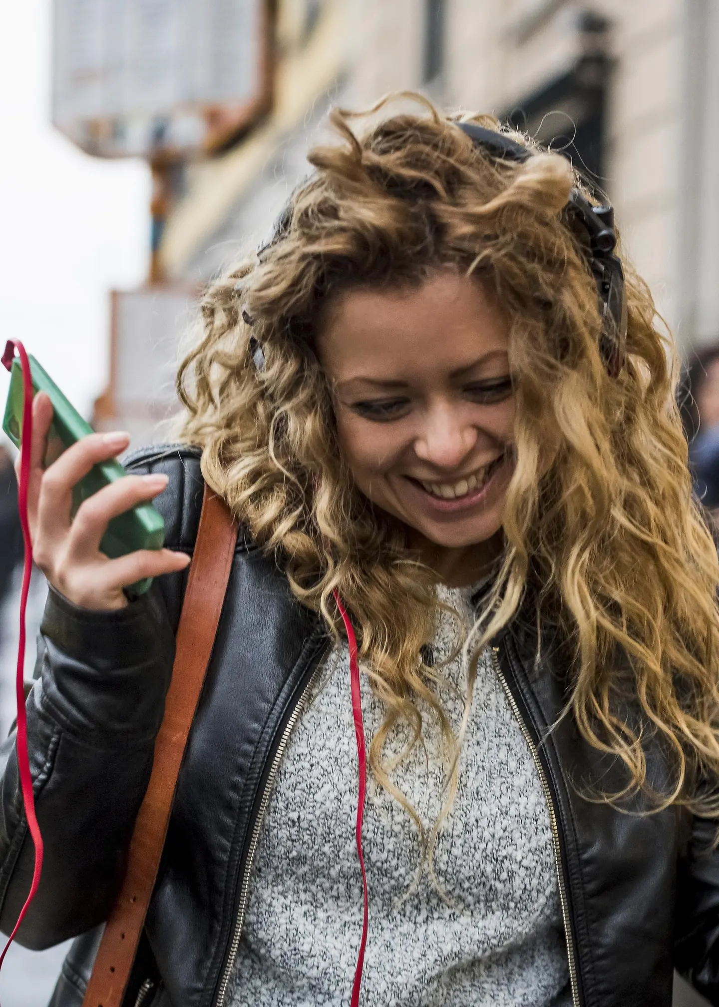 Una joven camina por la calle riendo y escuchando música en su móvil.
