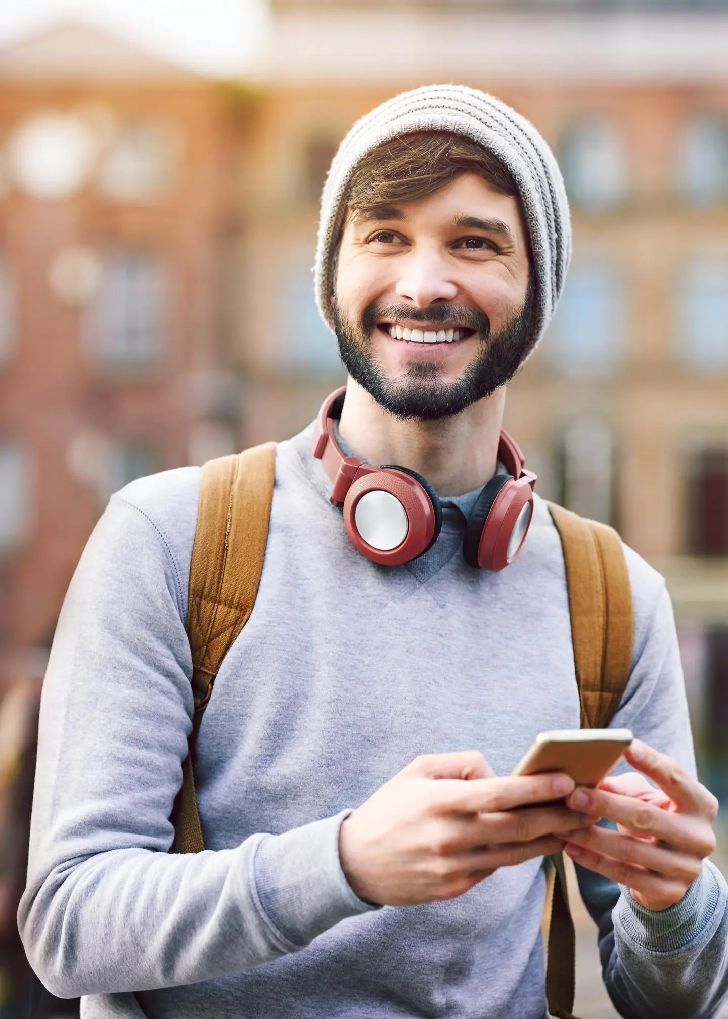 Un joven risueño con auriculares y un teléfono inteligente en la mano.