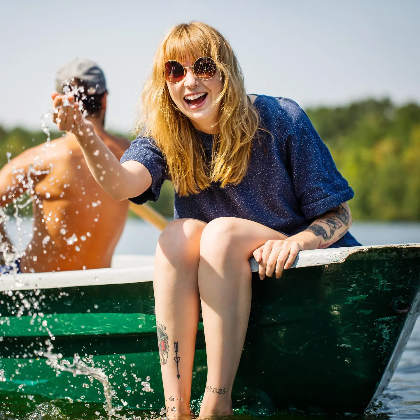 Una mujer joven sentada en un bote se ríe y salpica agua.