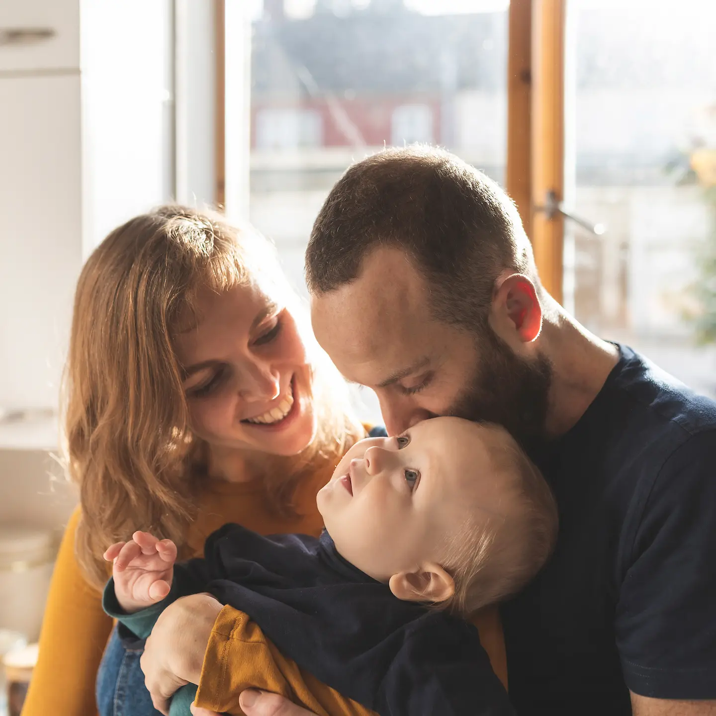 Junge Eltern stehen glücklich mit ihrem Baby im Arm in ihrer Küche