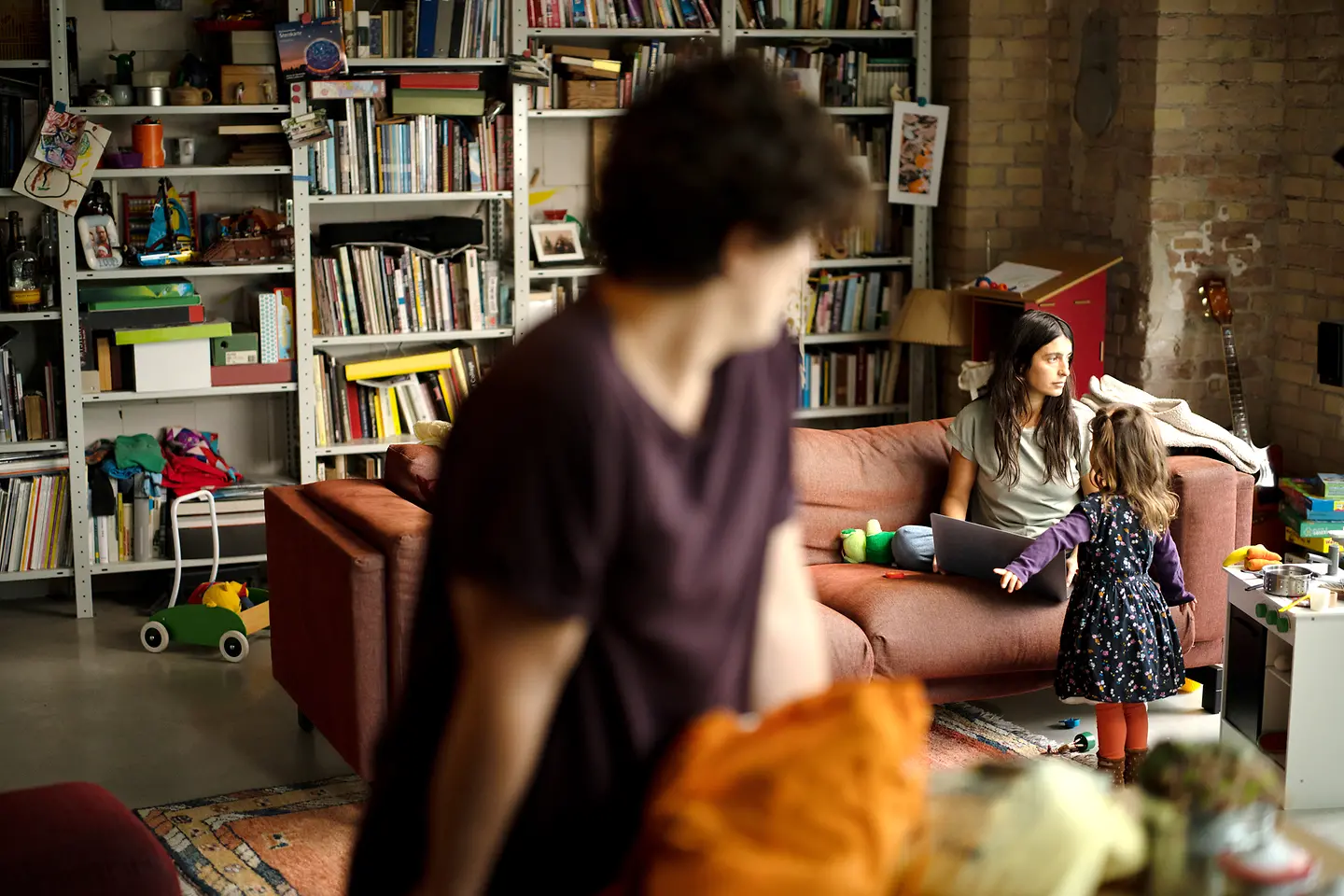 Familienszene: Die junge Mutter sitzt mit dem Notebook erschöpft auf der Couch und schaut zum Fenster raus.