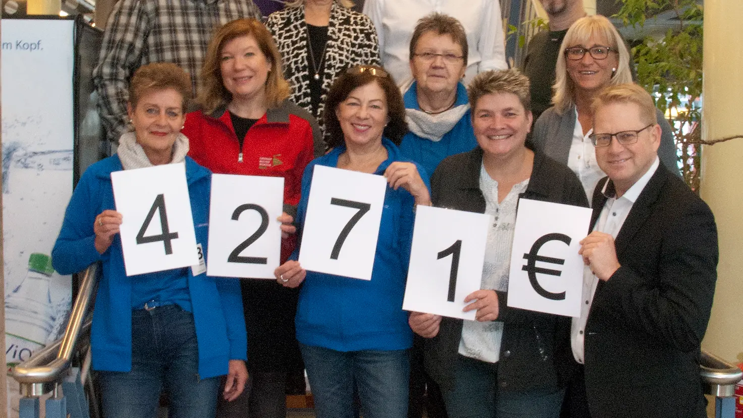 Mehrere Personen stehen auf einer Treppe für ein Gruppenfotos zusammen und halten die Zahlen 4271 € in den Händen.