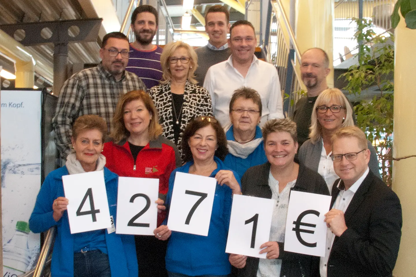 Mehrere Personen stehen auf einer Treppe für ein Gruppenfotos zusammen und halten die Zahlen 4271 € in den Händen.