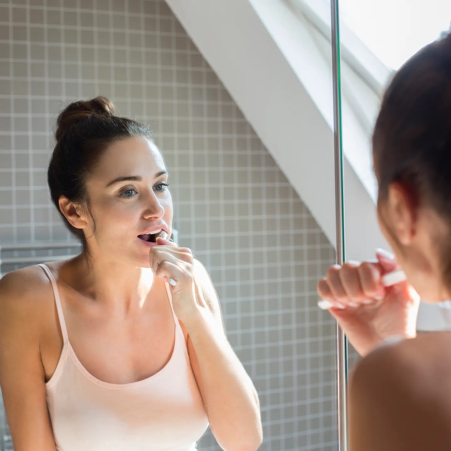 Junge Frau steht im Bad vor dem Spiegel und putzt sich die Zähne