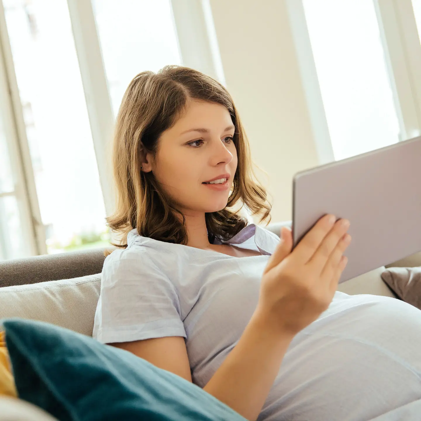 Junge schwangere Frau mit Tablet auf einer Couch