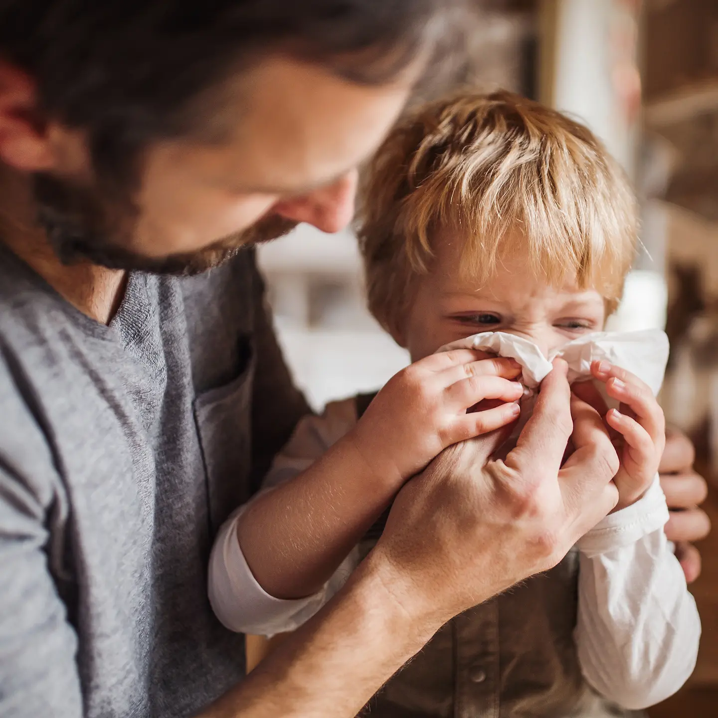 Ein Vater hilft seinem kleinen Jungen beim Naseputzen.