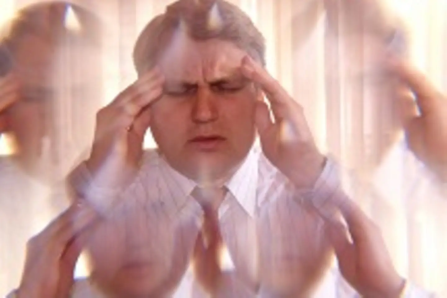 Ein Mann hat ein schmerzverzerrtes Gesicht und drückt sich die Finger an die Schläfen.