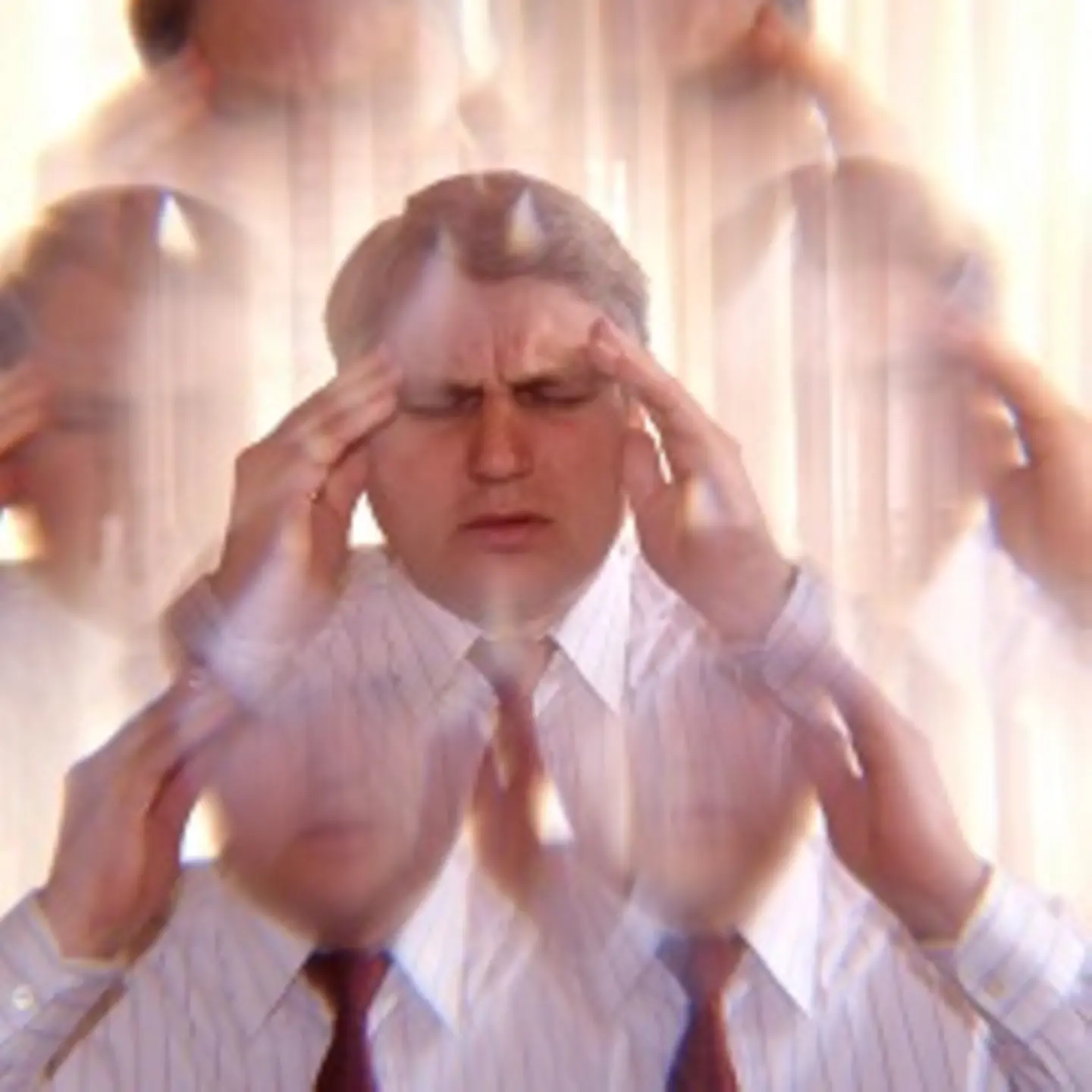 Ein Mann hat ein schmerzverzerrtes Gesicht und drückt sich die Finger an die Schläfen.