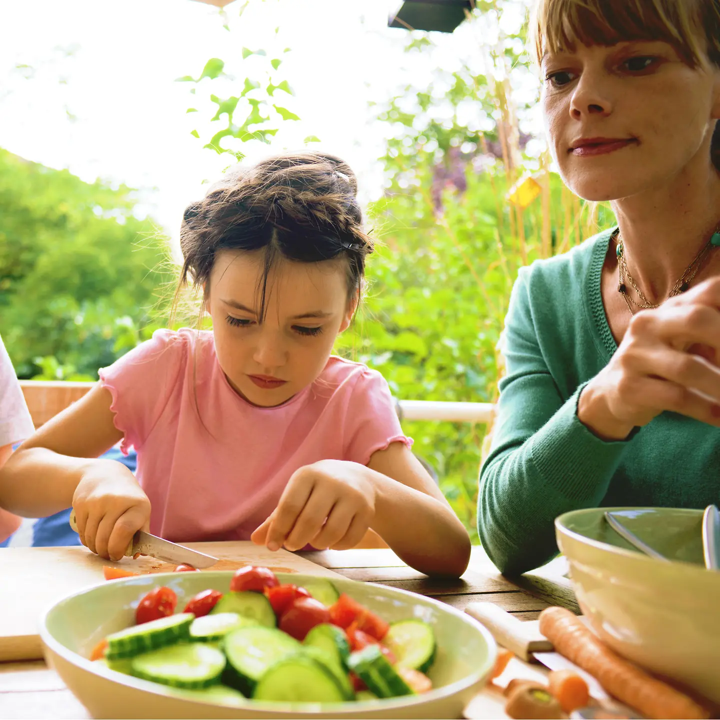 Eine Mutter und zwei Kinder sitzen an einem Tisch und schneiden Gemüse.