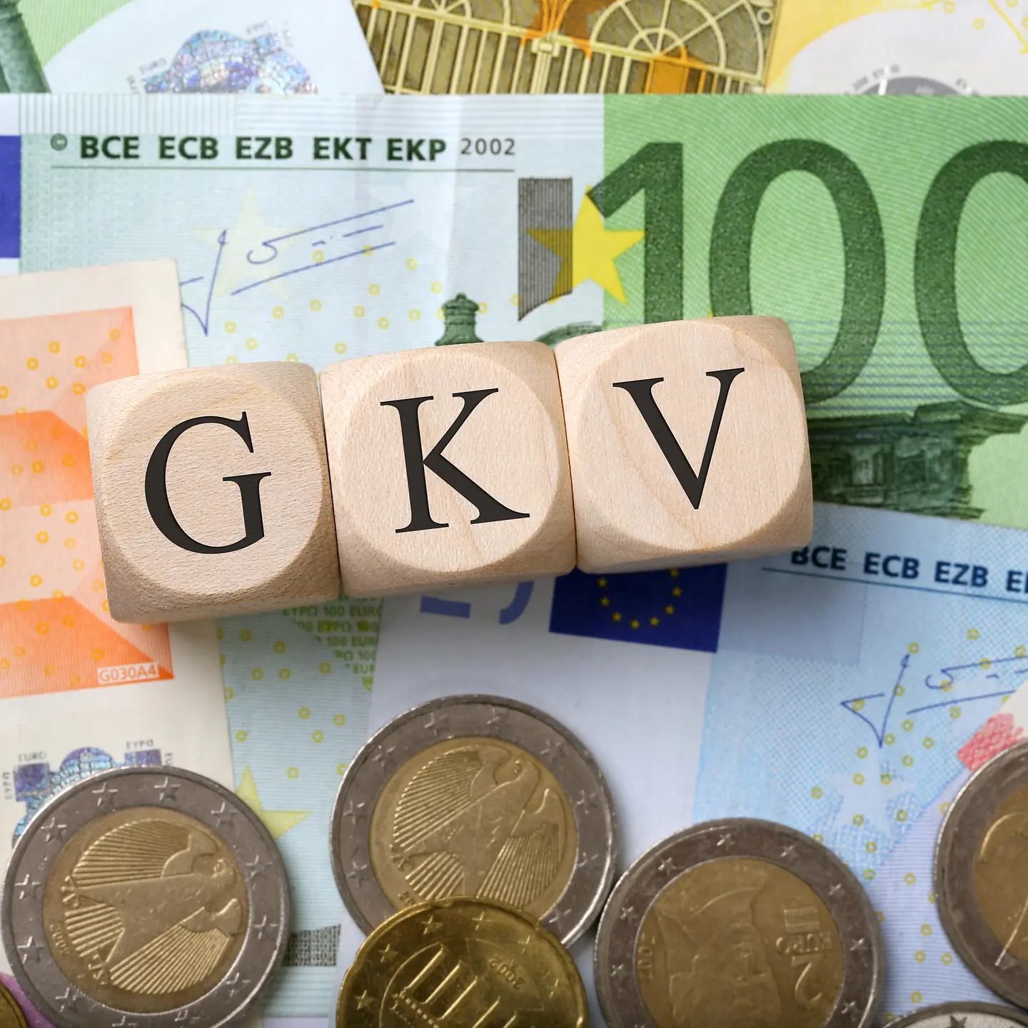 Das Bild zeigt verschiedene Euroscheine und Münzen auf denen drei Holzwürfel mit den Buchstaben GKV liegen.