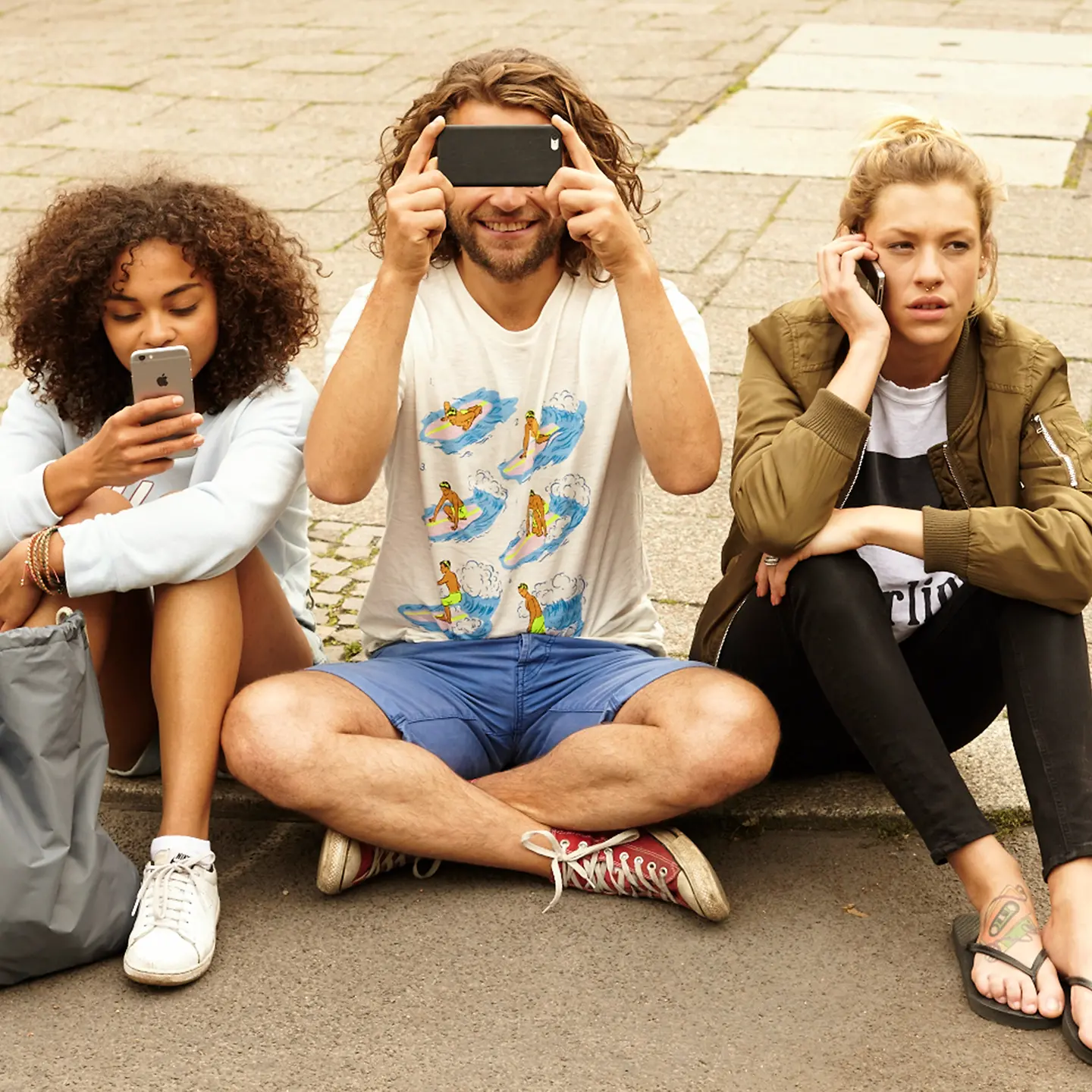 Drei junge Menschen sitzen mit ihren Smartphones auf dem Boden