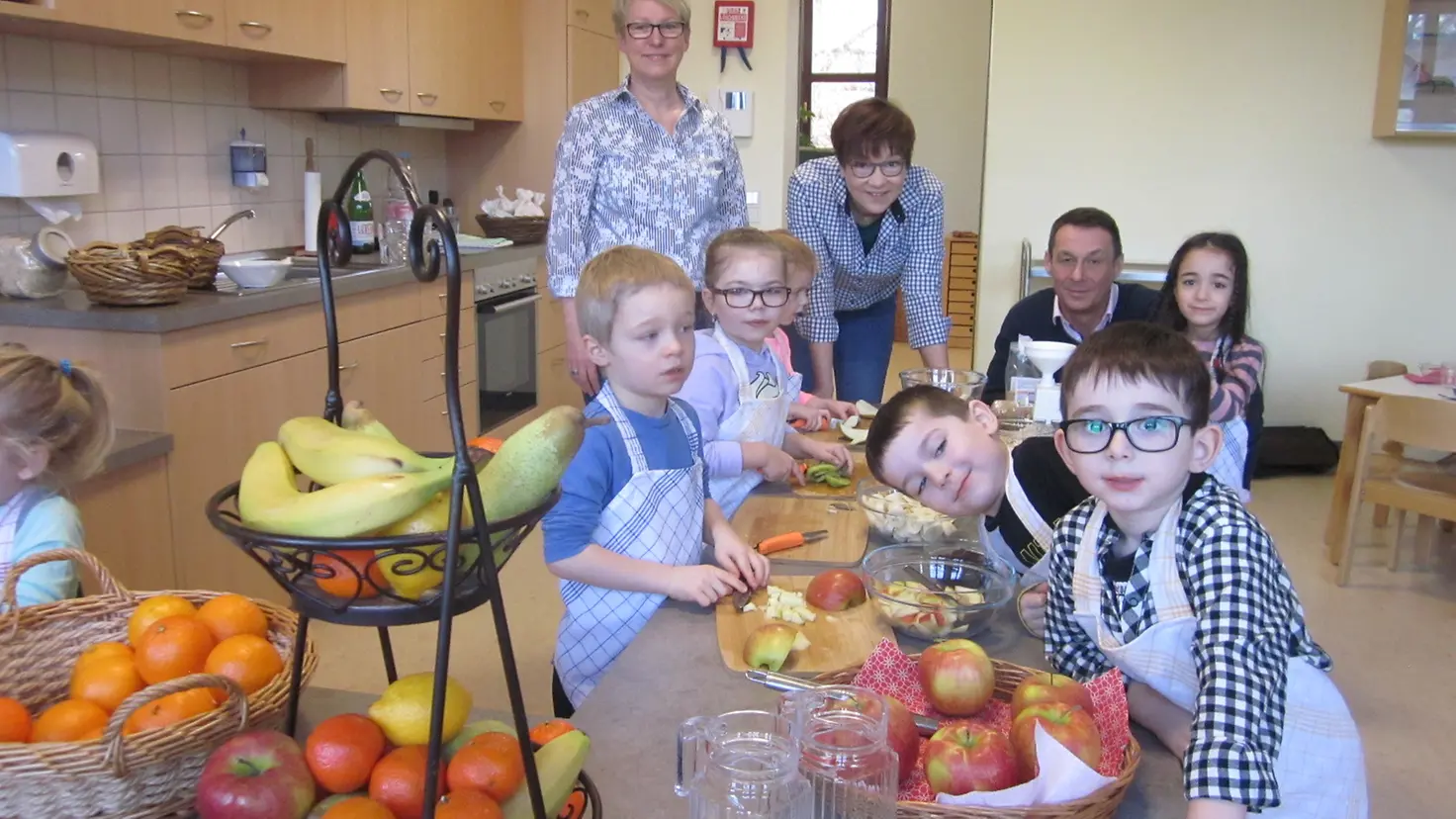 Kinder, Erzieher und BARMER-Vertreter in der Kita Küche beim Schnippeln von Gemüse.