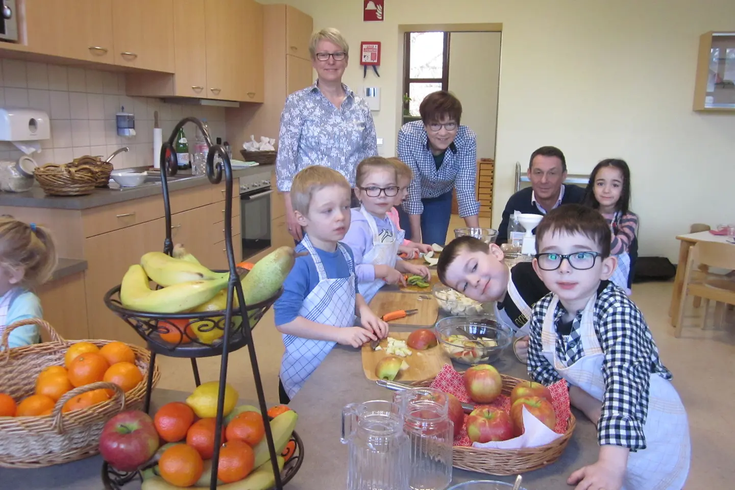 Kinder, Erzieher und BARMER-Vertreter in der Kita Küche beim Schnippeln von Gemüse.