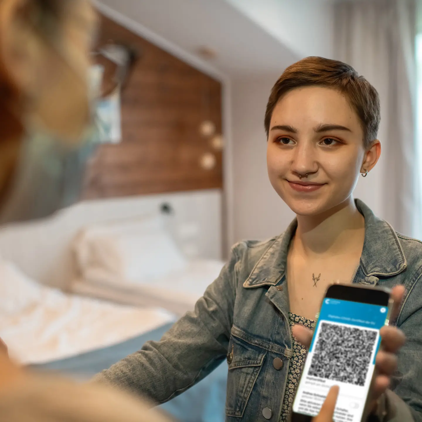 Junge Frau zeigt Covid-19-Impfpass und QR-Code auf dem Smartphone in einem Hotel