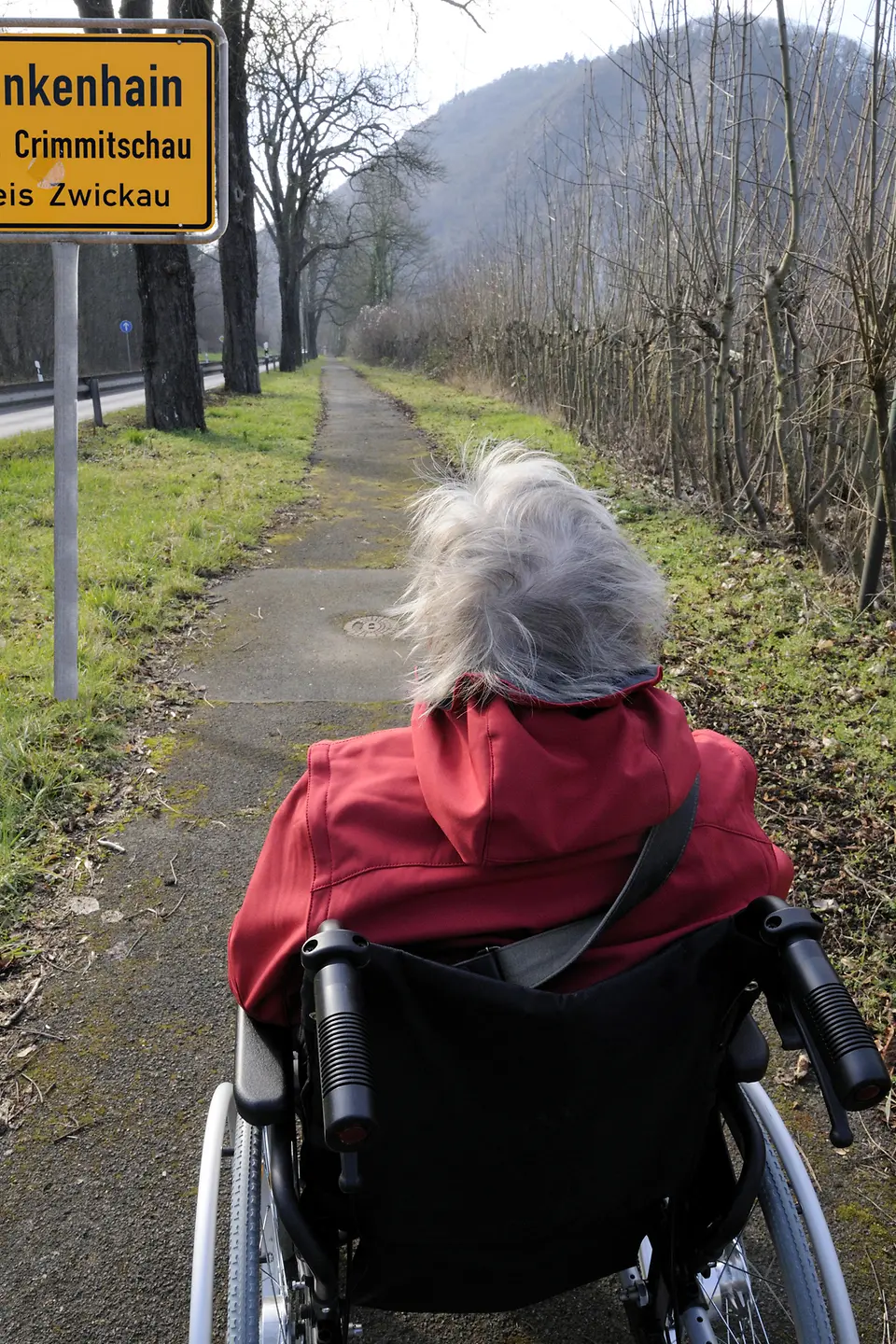 Frau im Rollstuhl fährt einen Weg entlang