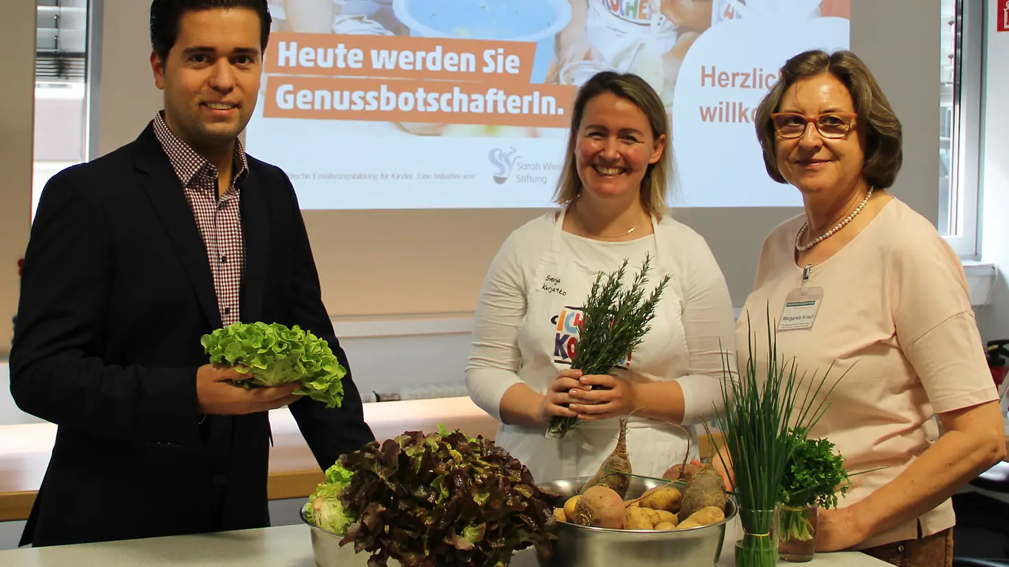 Dominik Bergemann, Fortbildungsleiterin Kurjatko und Maragarete Knauf vor einer Wand mit Gemüse in der Hand.
