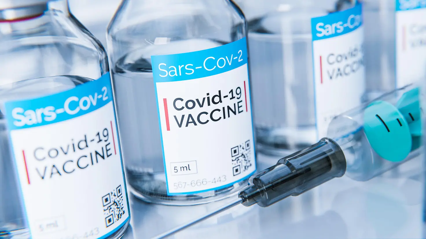 Das Bild zeigt Fläschchen mit Corona-Impfstoff neben einer Spritze.