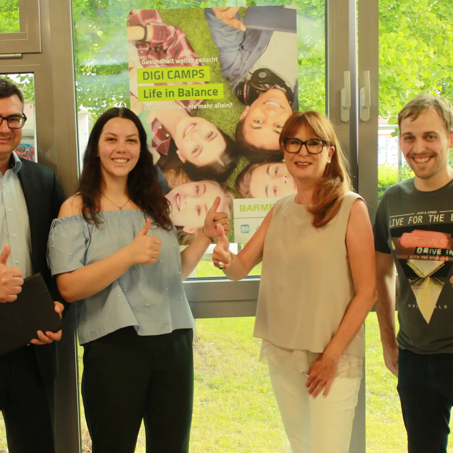 Zwei der Veranstalter mit eine Schülerin und einem Lehrer vor einer Wand.