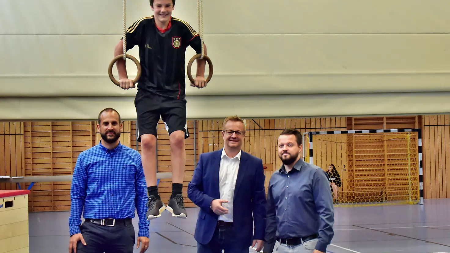 Ein Schüler balanciert in Ringen, zwei Lehrer und Jörg Peter (BARMER) stehen daneben.
