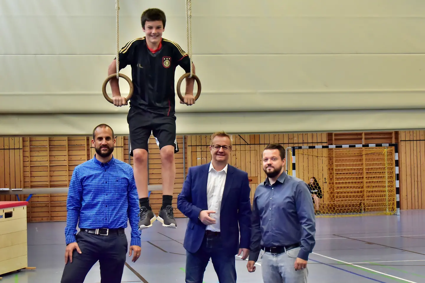 Ein Schüler balanciert in Ringen, zwei Lehrer und Jörg Peter (BARMER) stehen daneben.