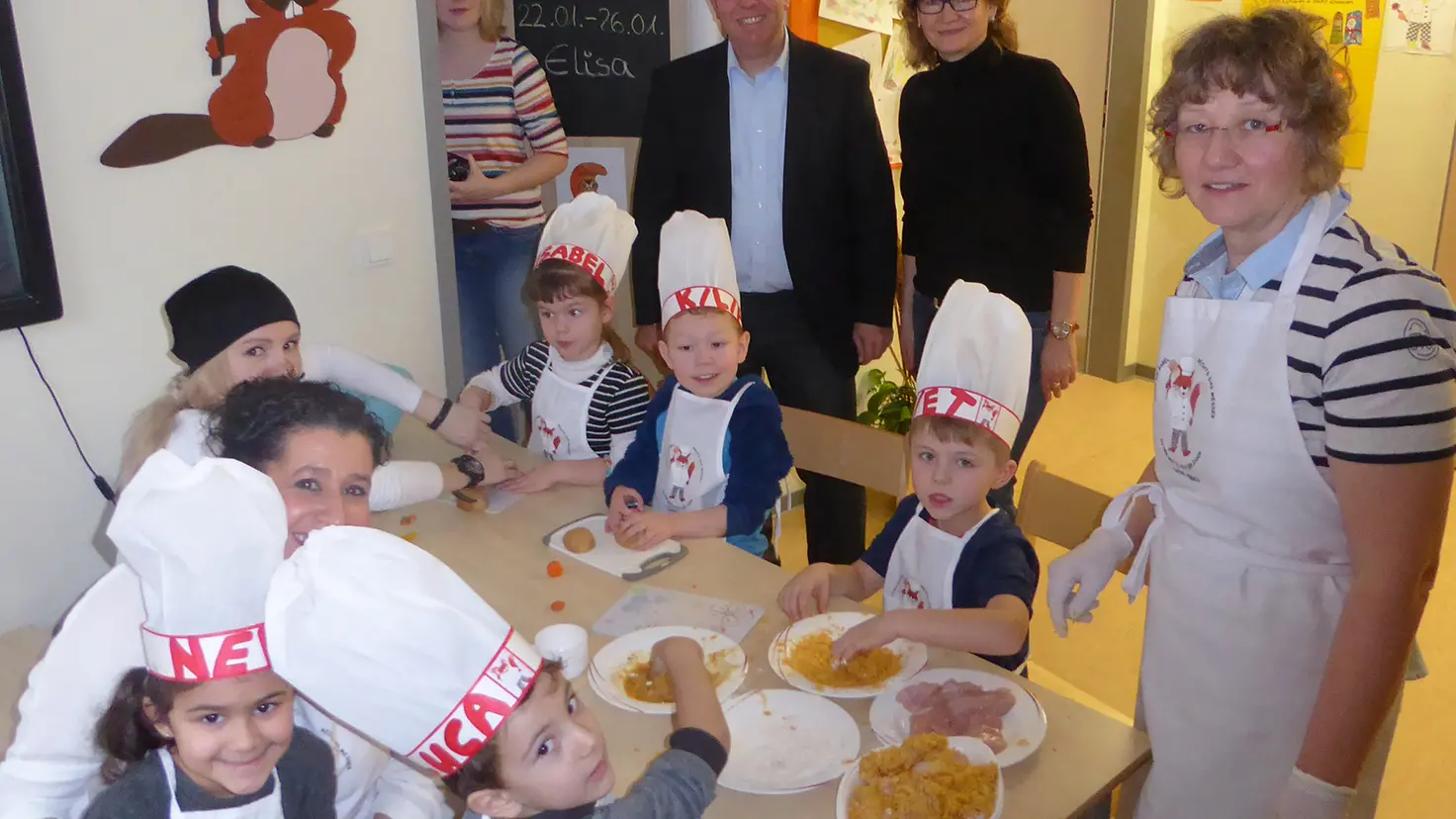 KITA-Kinder sitzen am Tisch und bereiten Essen mit KITA-Mitarbeiterinnen zu. Im Hintergrund: Oliver Hellriegel.