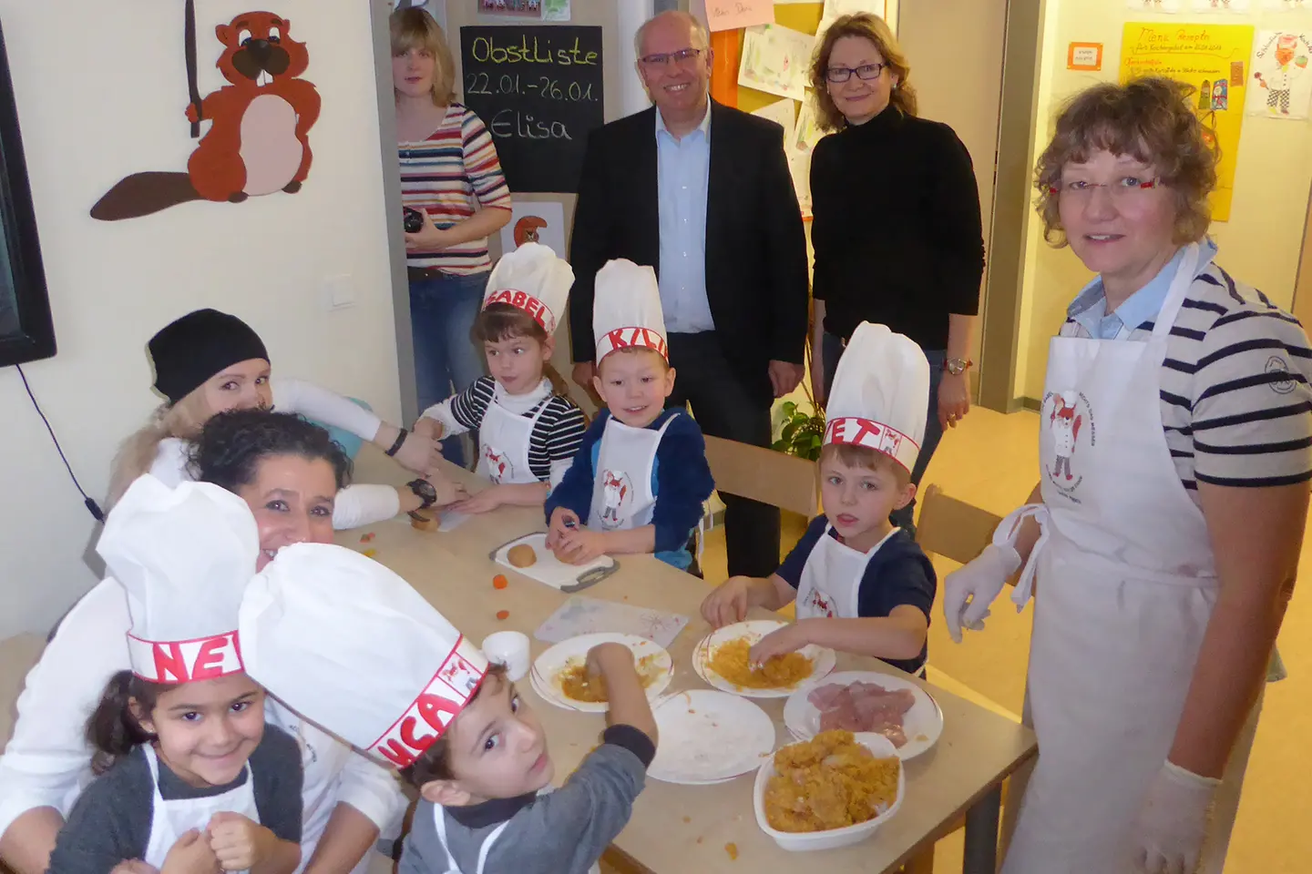 KITA-Kinder sitzen am Tisch und bereiten Essen mit KITA-Mitarbeiterinnen zu. Im Hintergrund: Oliver Hellriegel.