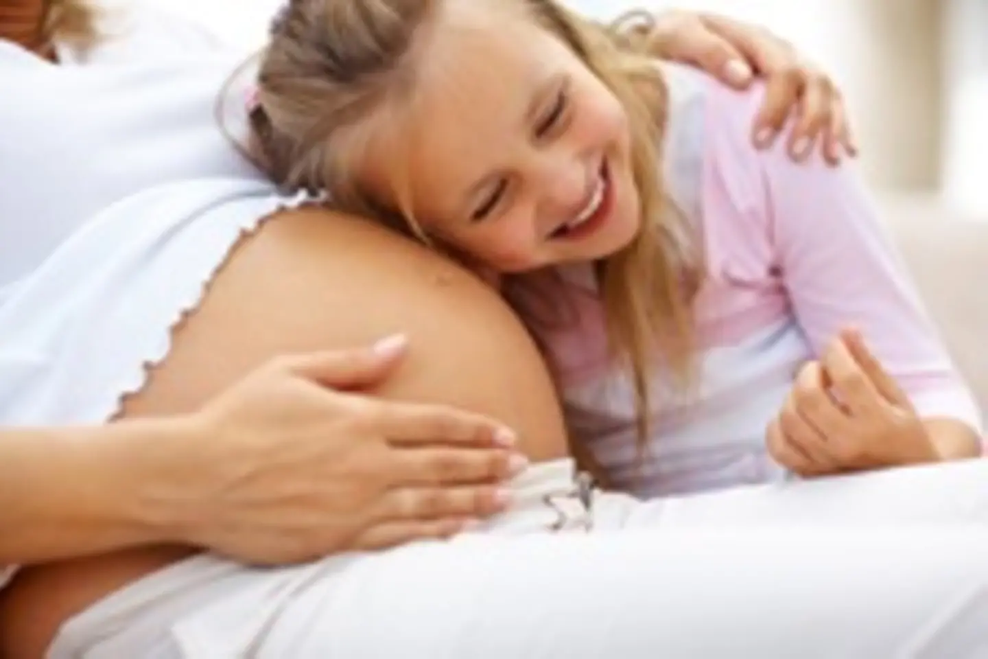 Ein kleines Mädchen liegt liegend mit ihrem Kopf auf dem Bauch einer schwangeren Frau.