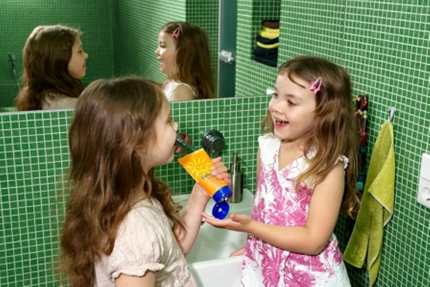 Zwei kleine Mädels cremen sich mit der Sonnencreme ein.