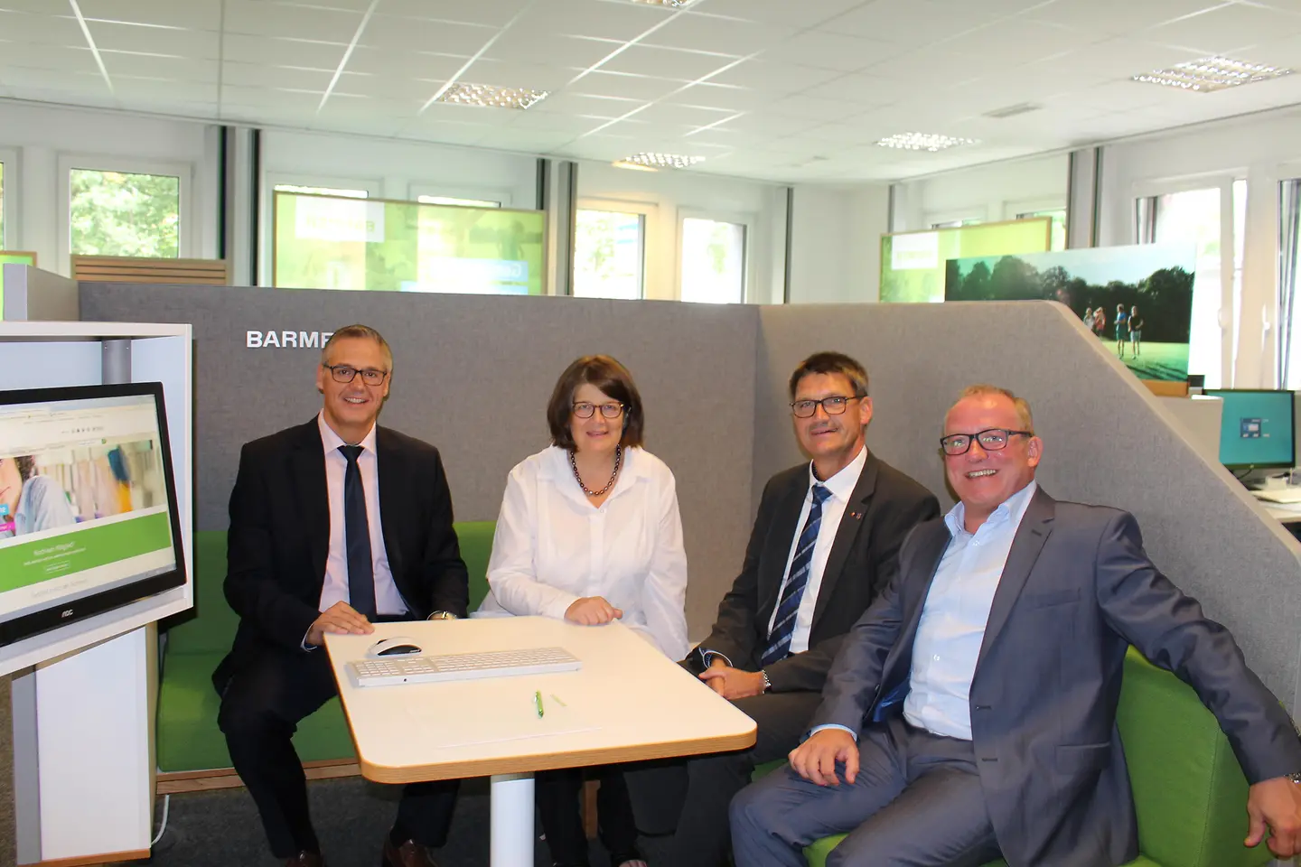 Barmer Mitarbeiter, die Trierer Bürgermeisterin und der Landrat des Kreises Trier-Saarburg sitzen Probe in einer Beratungsbox.