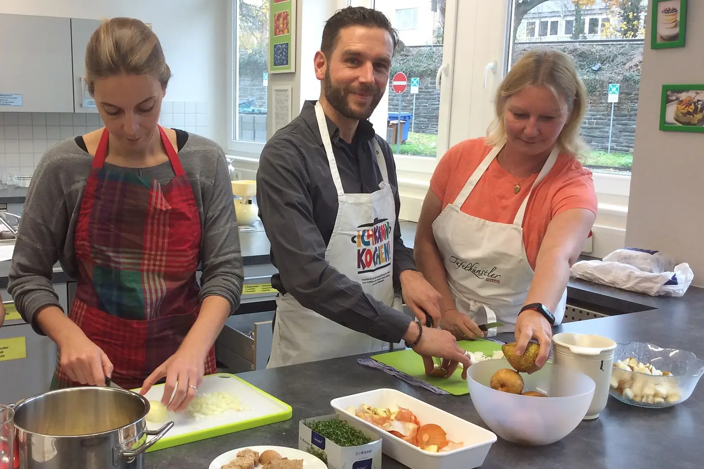 Trainer Stefan Brandel in der VHS-Lehrküche mit Pädagoginnen beim Zubereiten von Speisen.