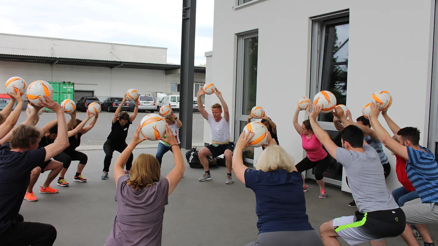 Jonas Reckermann wärmt Mitarbeiter von JF Hillebrand mit Beachvolleyball-Übungen auf.