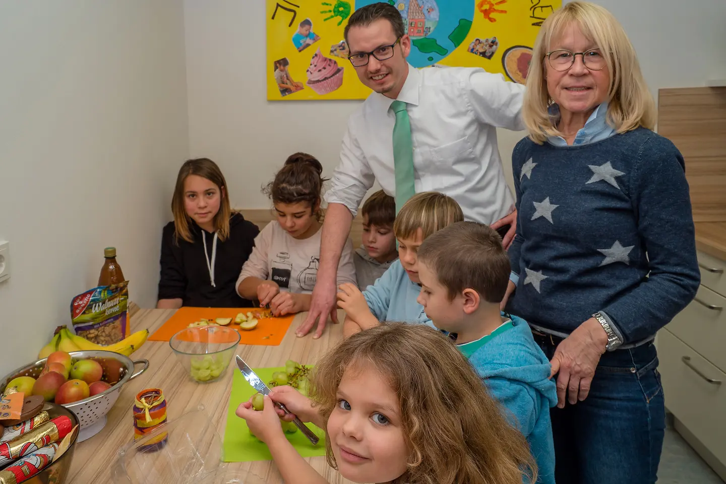 Kinder schneiden Obst an einem Tisch zusammen mit Martin Herz und Adelheid Theisinger.