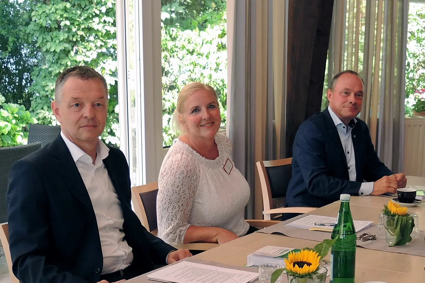 Drei Personen sitzen an einem Tisch und lächeln in die Kamera