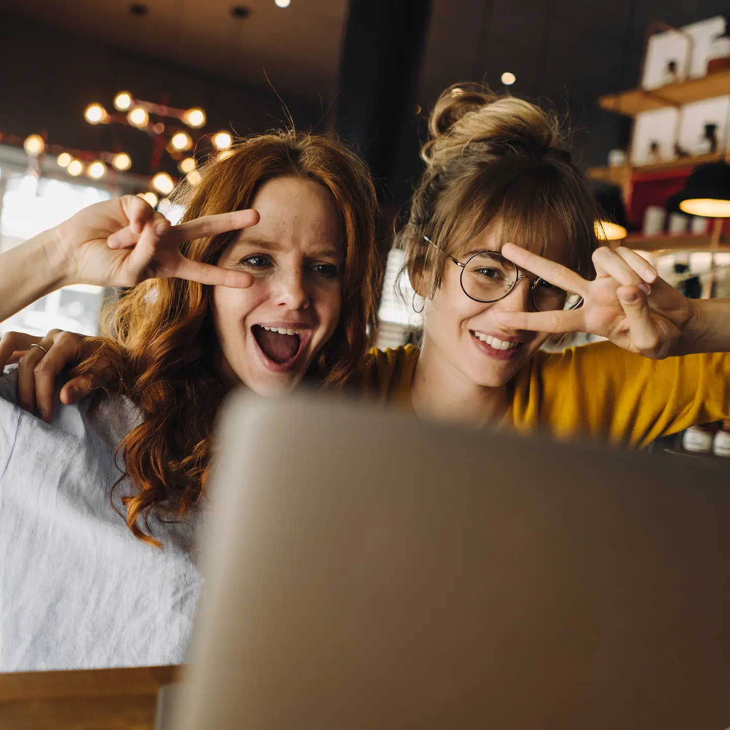 Zwei fröhliche junge Frauen an einem Laptop in einem Cafe