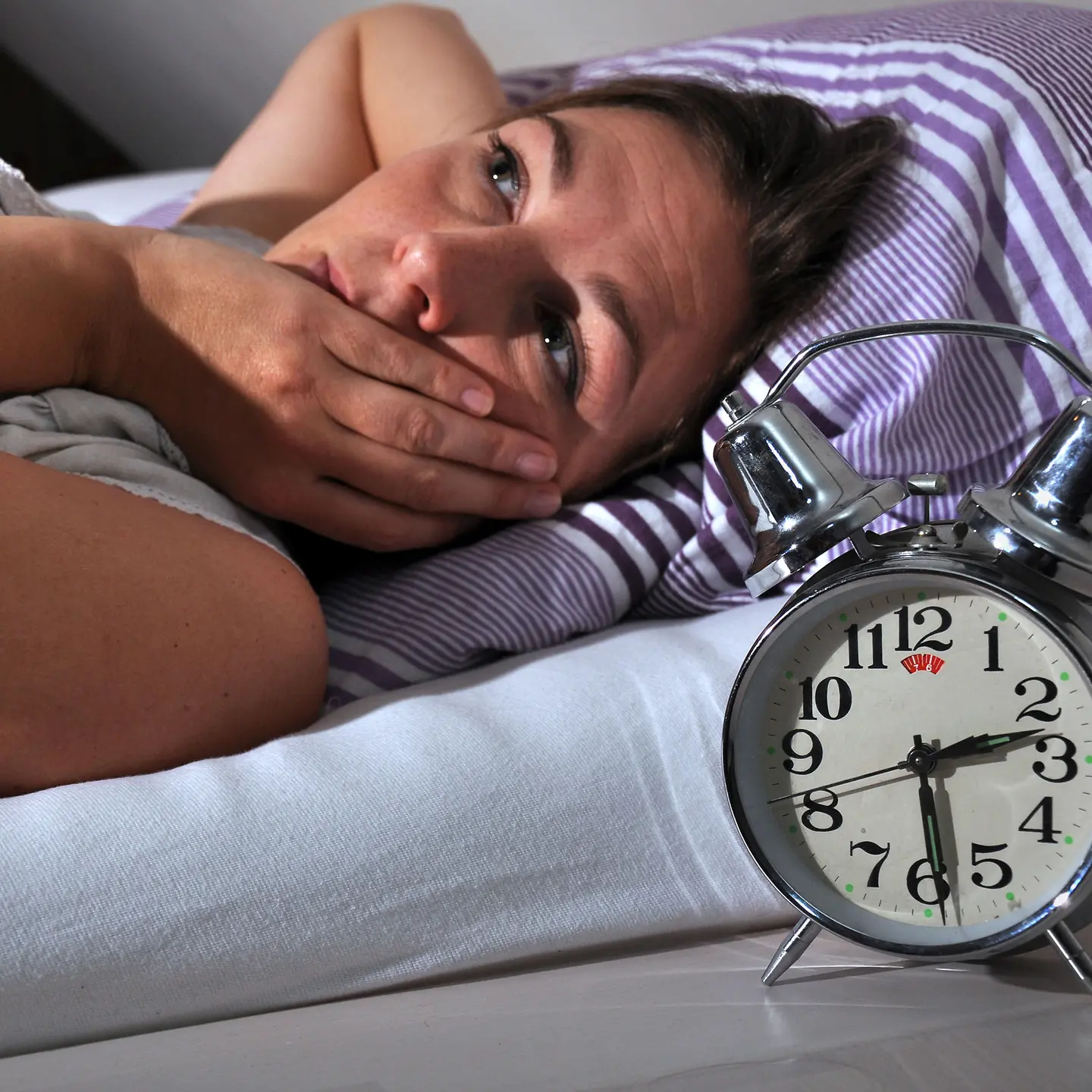 Eine Frau liegt schlaflos im Bett. Der Wecker neben dem Bett zeigt halb 3 an.