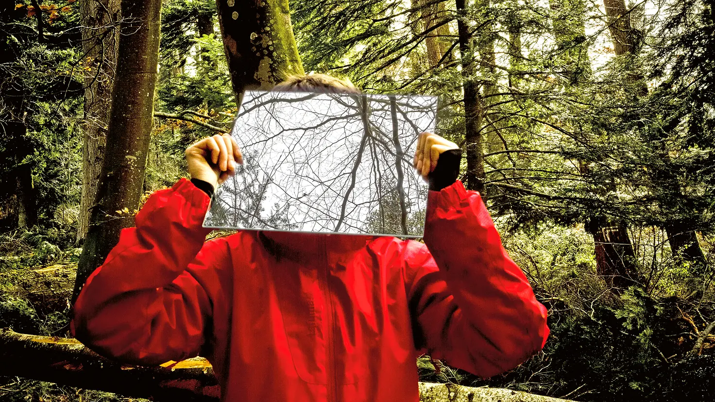 Eine Person steht im Wald und hält sich einen Spiegel vor das Gesicht