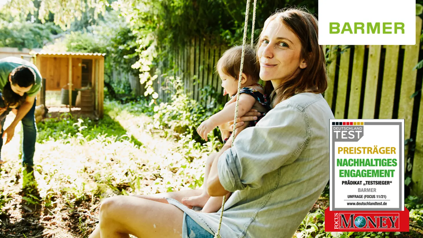 Ein junges Elternpaar mit zwei Kleinkindern spielt und schaukelt in einem Garten.