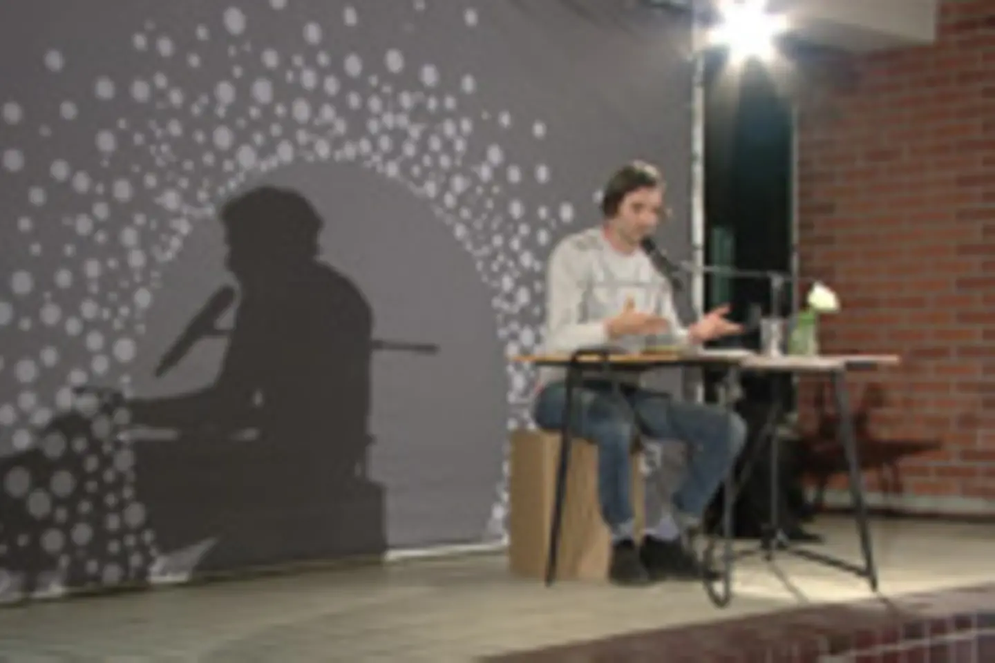 Eine Person sitzt an einem Tisch auf einer Bühne