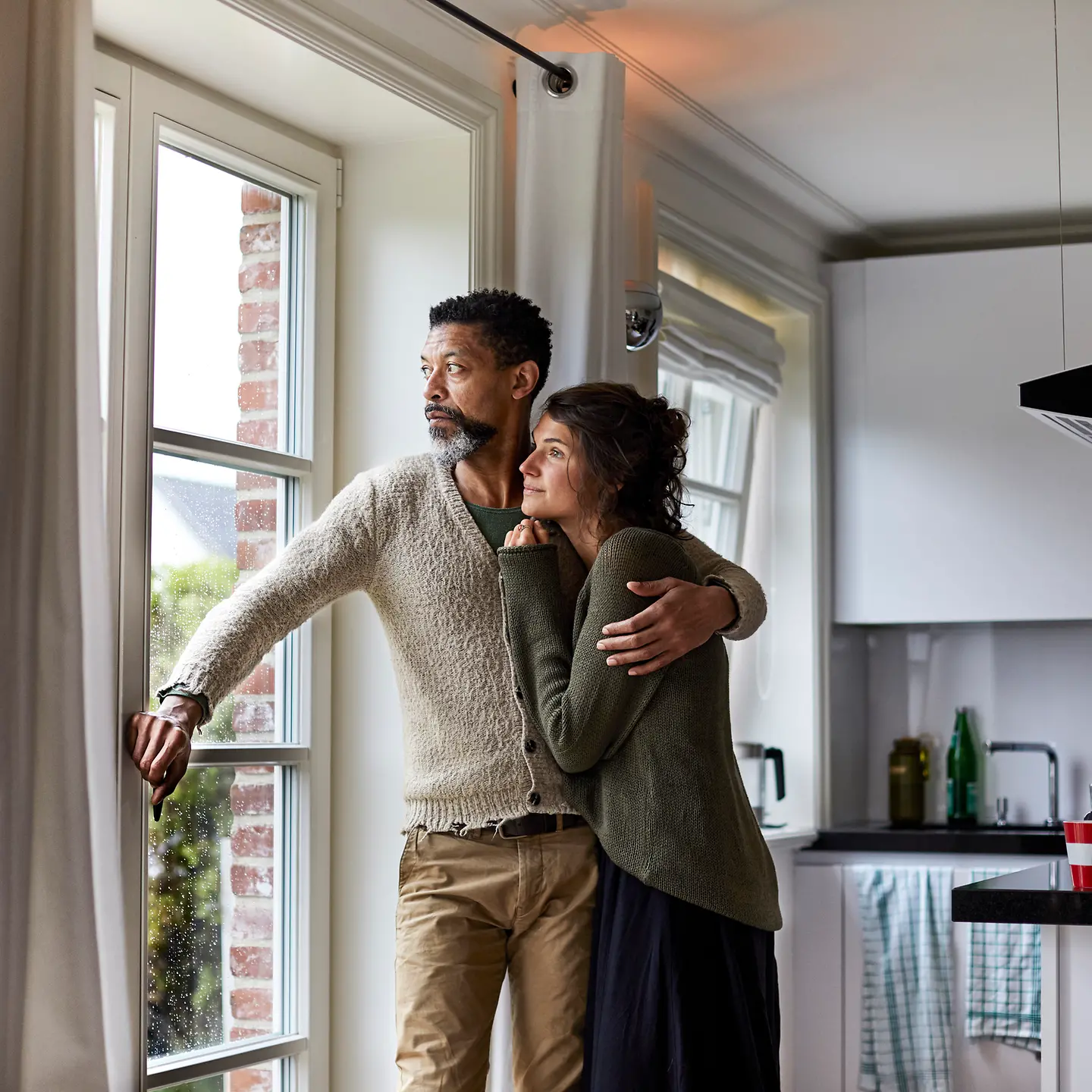 Ernster Mann umarmt eine Frau, sie schauen aus einem Fenster