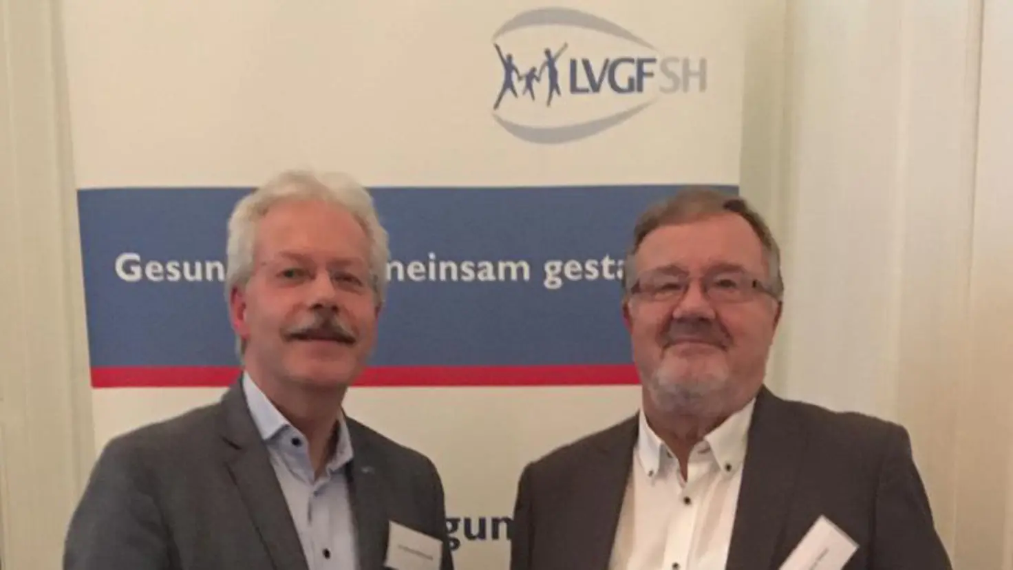 Dr. Bernd Hillebrandt und Dietmar Katzer stehend vor einem Display der LVGF-SH