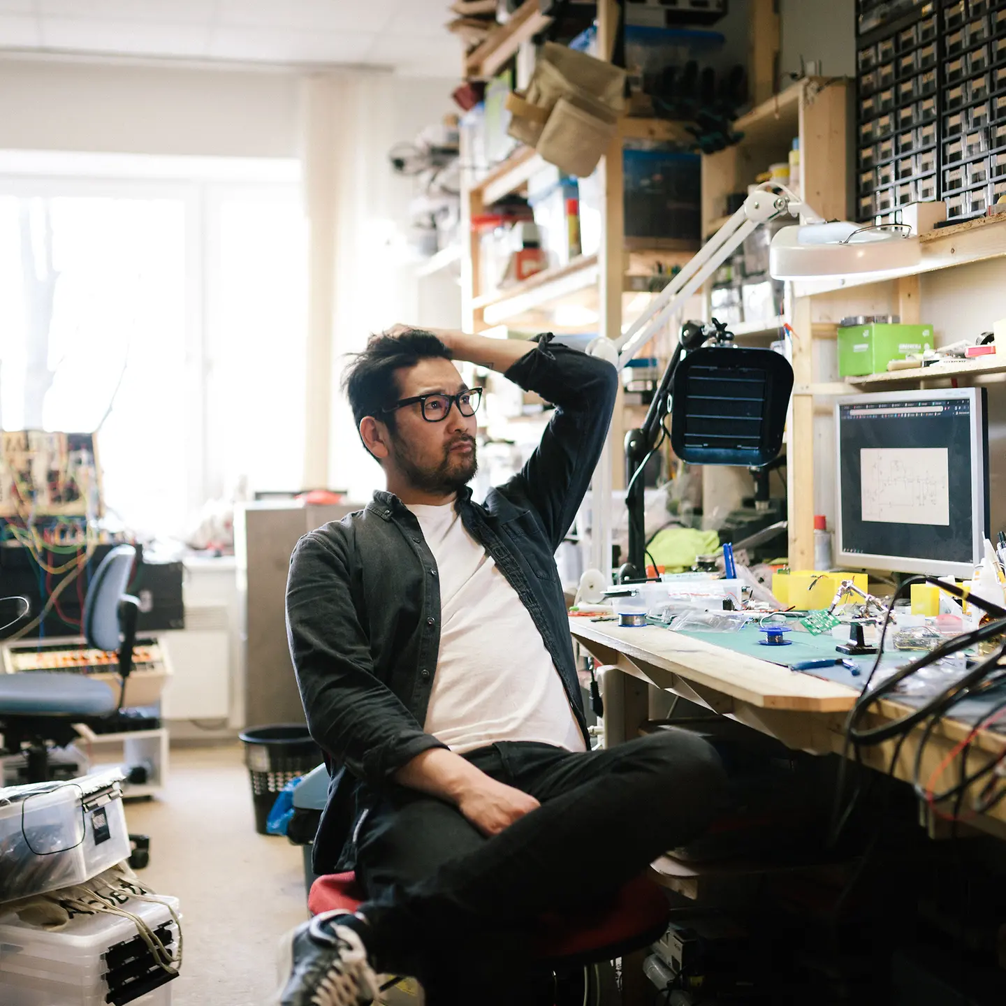 Ein junger Mann sitzt in einem Büro mit viel Technik-Equipment