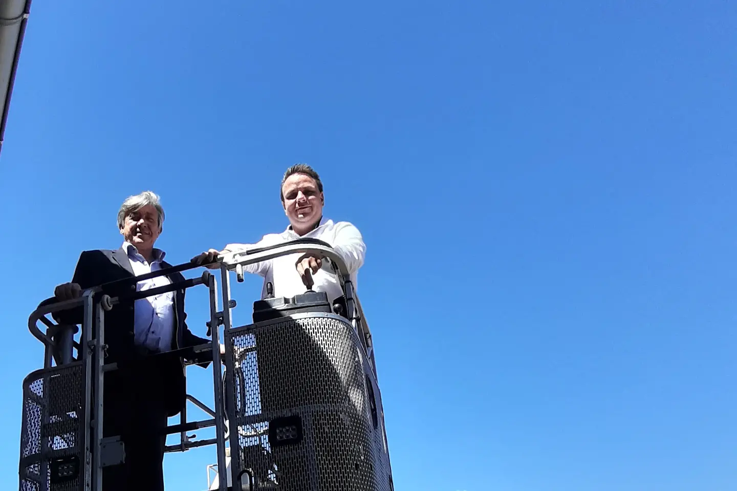 Zwei Personen stehen oben im Korb auf einer Drehleiter eines Einsatzfahrzeuges und schauen in die Kamera.